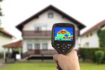 Thermografie-Messgerät mit Wärmebild. Im Hintergrund ist ein unscharfes Haus zu erkennen